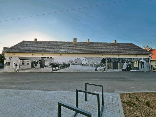 28‑metrowy mural na ul. Reymonta w Dobrzeniu Wielkim — sceny z życia dawnej miejscowości, budynki i postacie z archiwalnych fotografii.